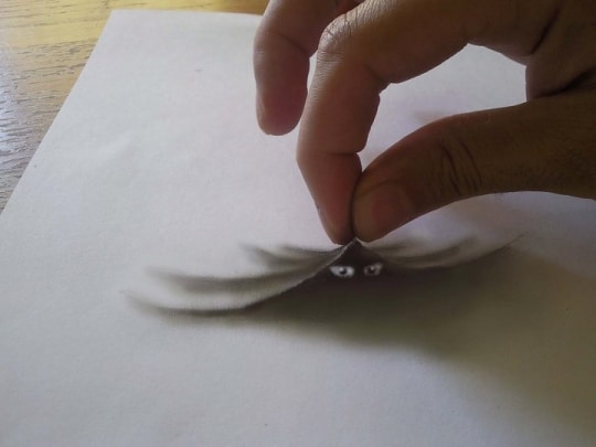 Un effet de pliure dans la feuille provoquée par la main du dessinateur, deux yeux apparaissent en-dessous.