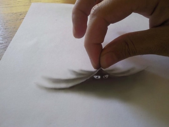 Un effet de pliure dans la feuille provoquée par la main du dessinateur, deux yeux apparaissent en-dessous.