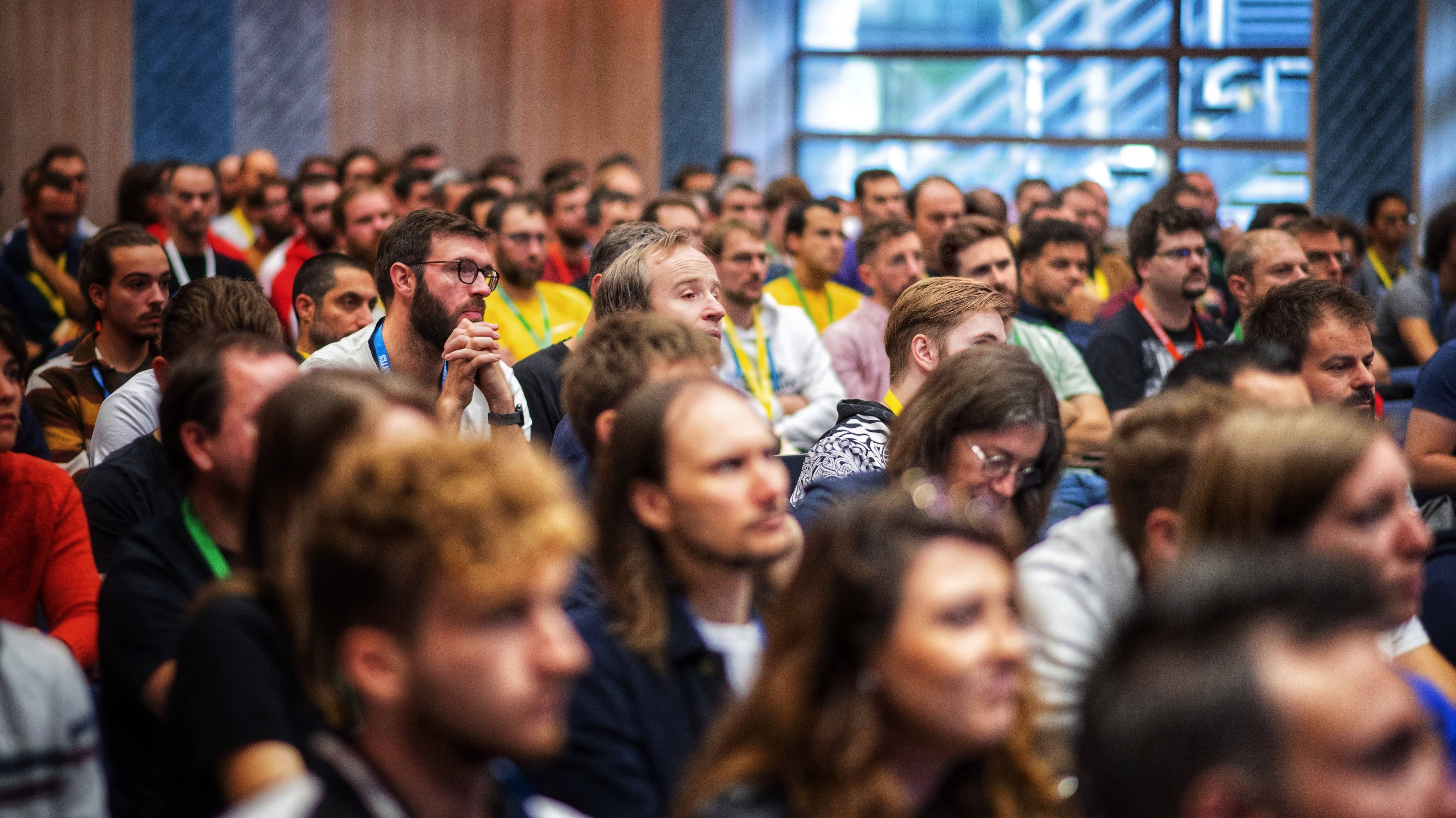 Différents profils attentifs au conférencier en train de parler : freelance, dirigeant, employé, etc. On voit clairement une salle comble.